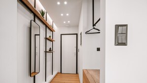 A hallway with a wooden floor, white walls, a door, a mirror, a shelf with plants, and a bench. - Plānis Str Urban Suites by Semavi (Heraklion)