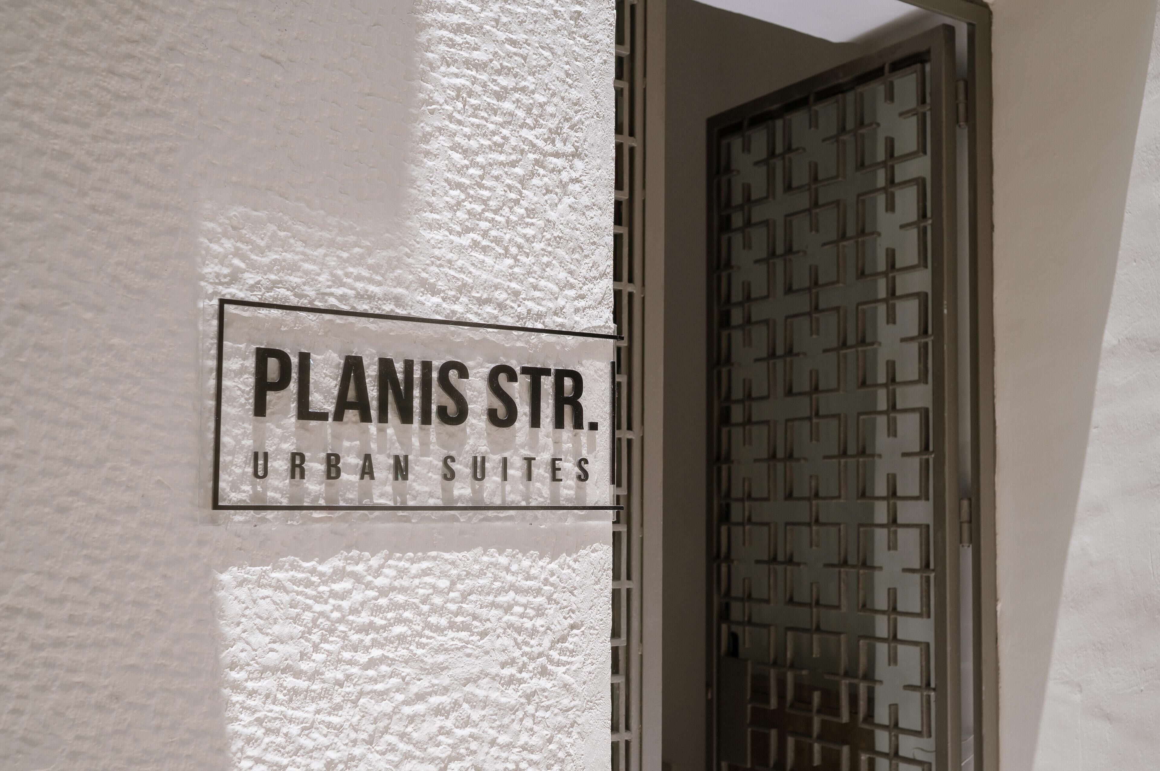 Een bord met de tekst 'PLANIS STR. URBAN SUITES' op een structuurwand.