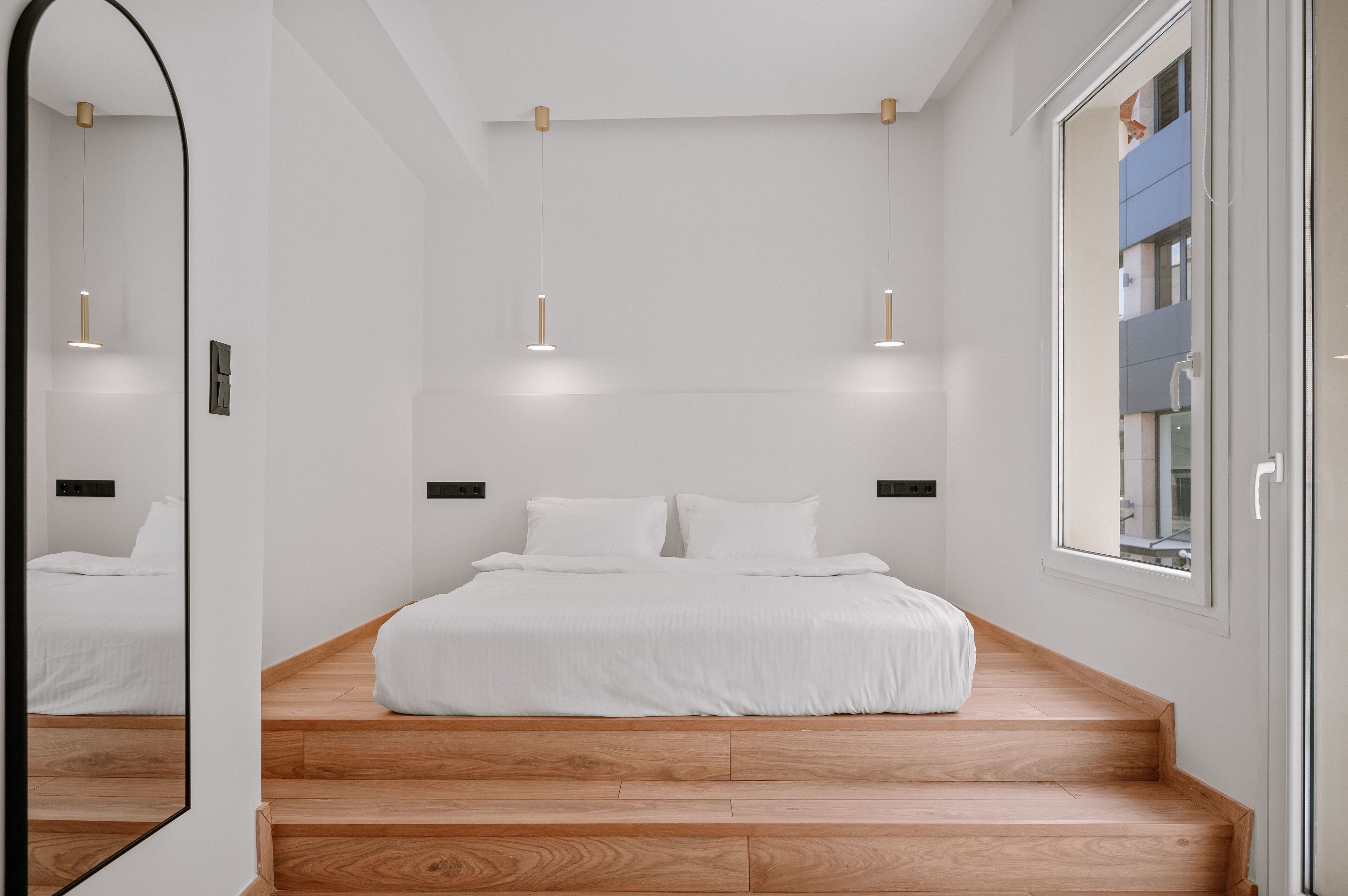 Un dormitorio moderno con escalera de madera, cama grande e iluminación colgante.