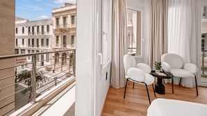 A balcony with a view of a building labeled 'Londos Center'. Inside, there is a seating area with two white chairs and a small table with a plant. - Plānis Str Urban Suites by Semavi (Heraklion)