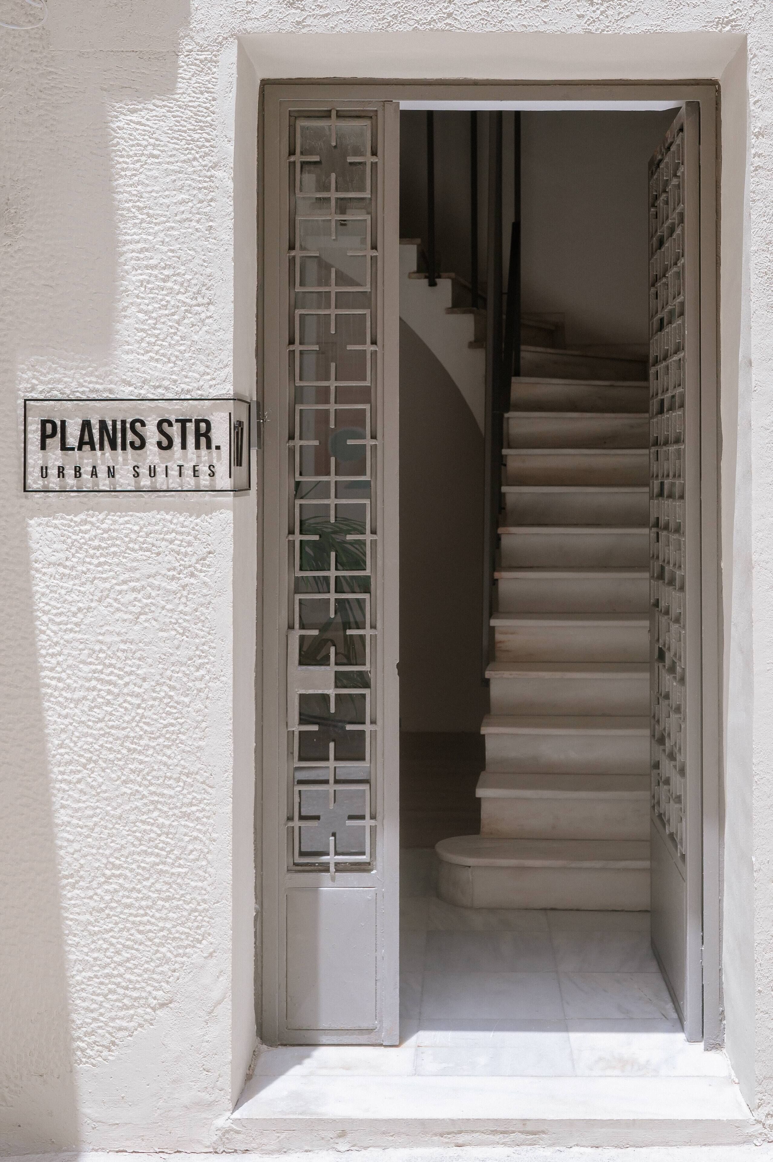 Eine Treppe führt zu einer oberen Etage, mit einem Schild, auf dem 'Planis Str. Urban Suites' steht.