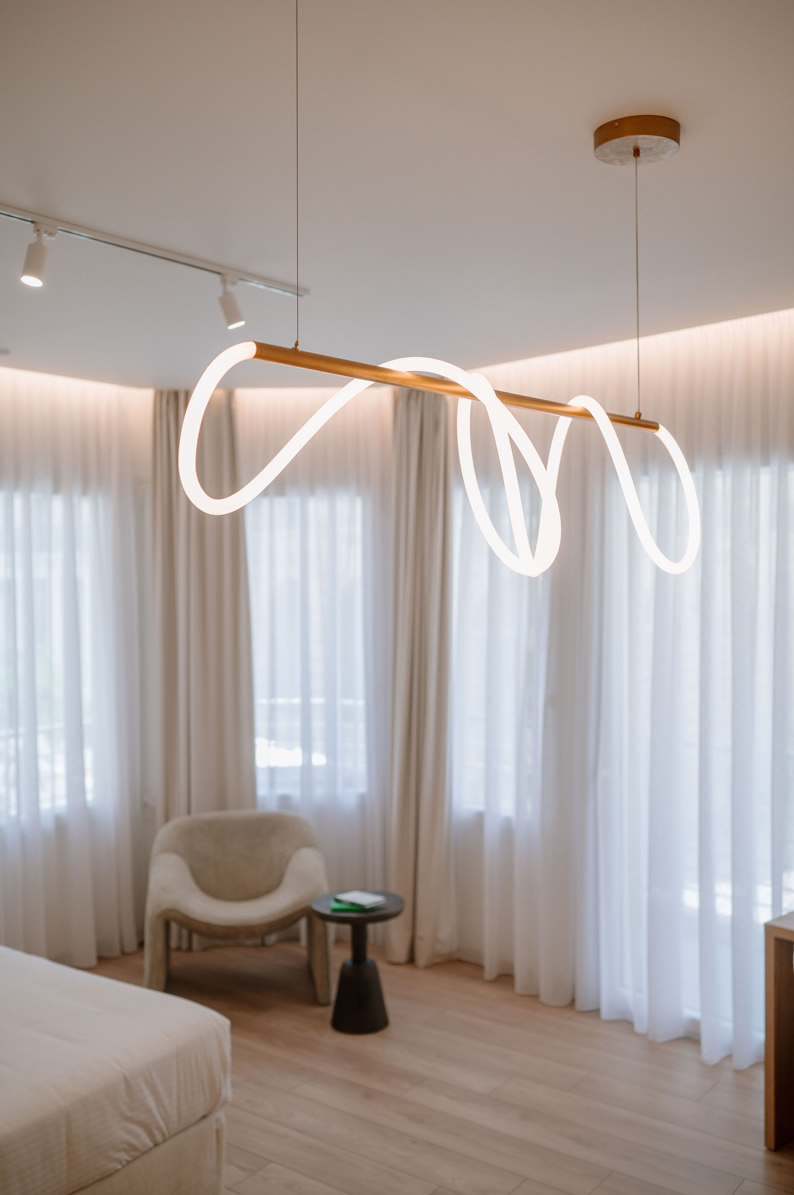 A modern hotel room with a large bed, a chair, a small table, and a unique light fixture.