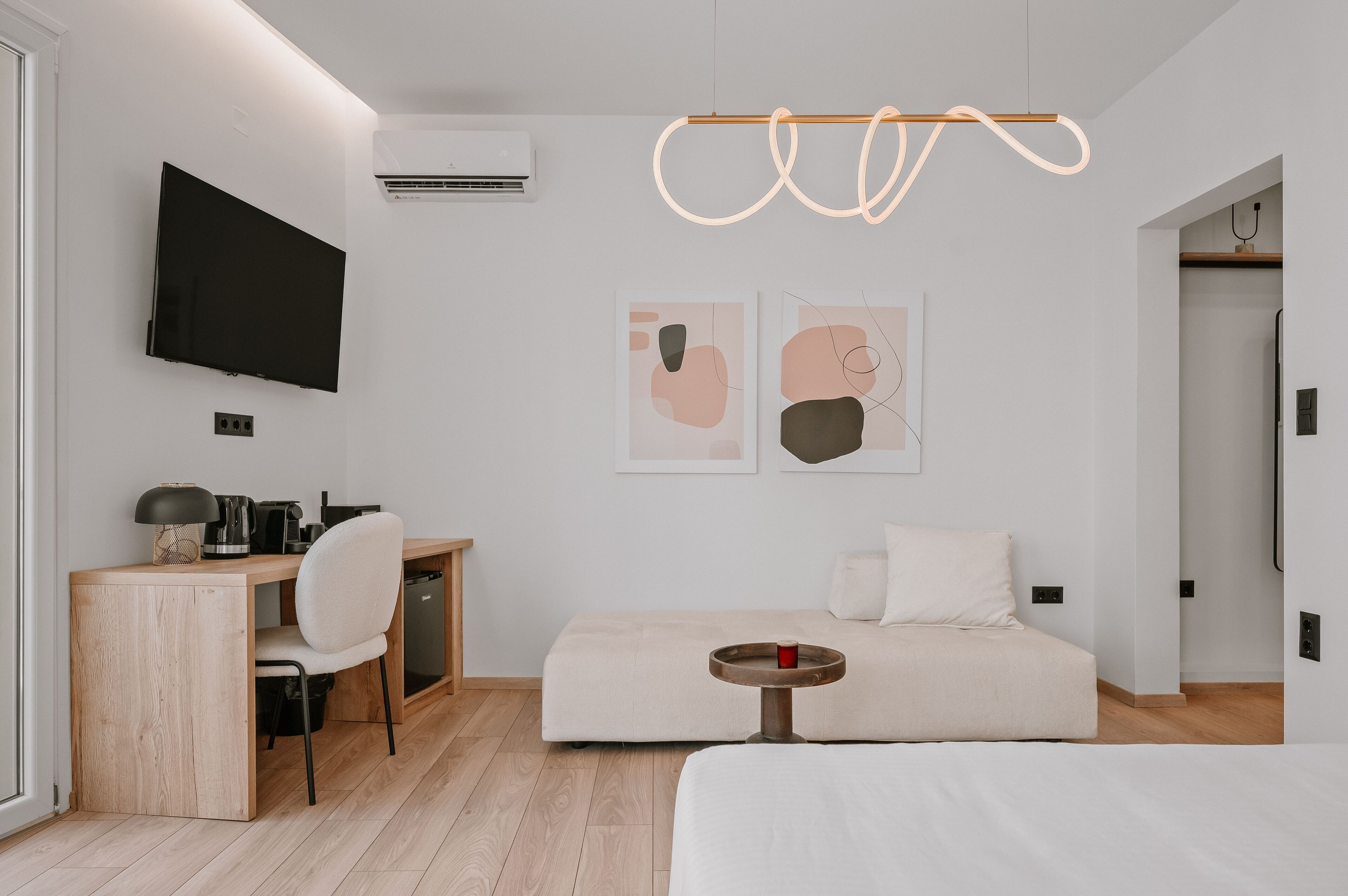 Quarto de hotel moderno e minimalista com uma escrivaninha de madeira, uma cama e uma televisão de tela plana presa à parede.