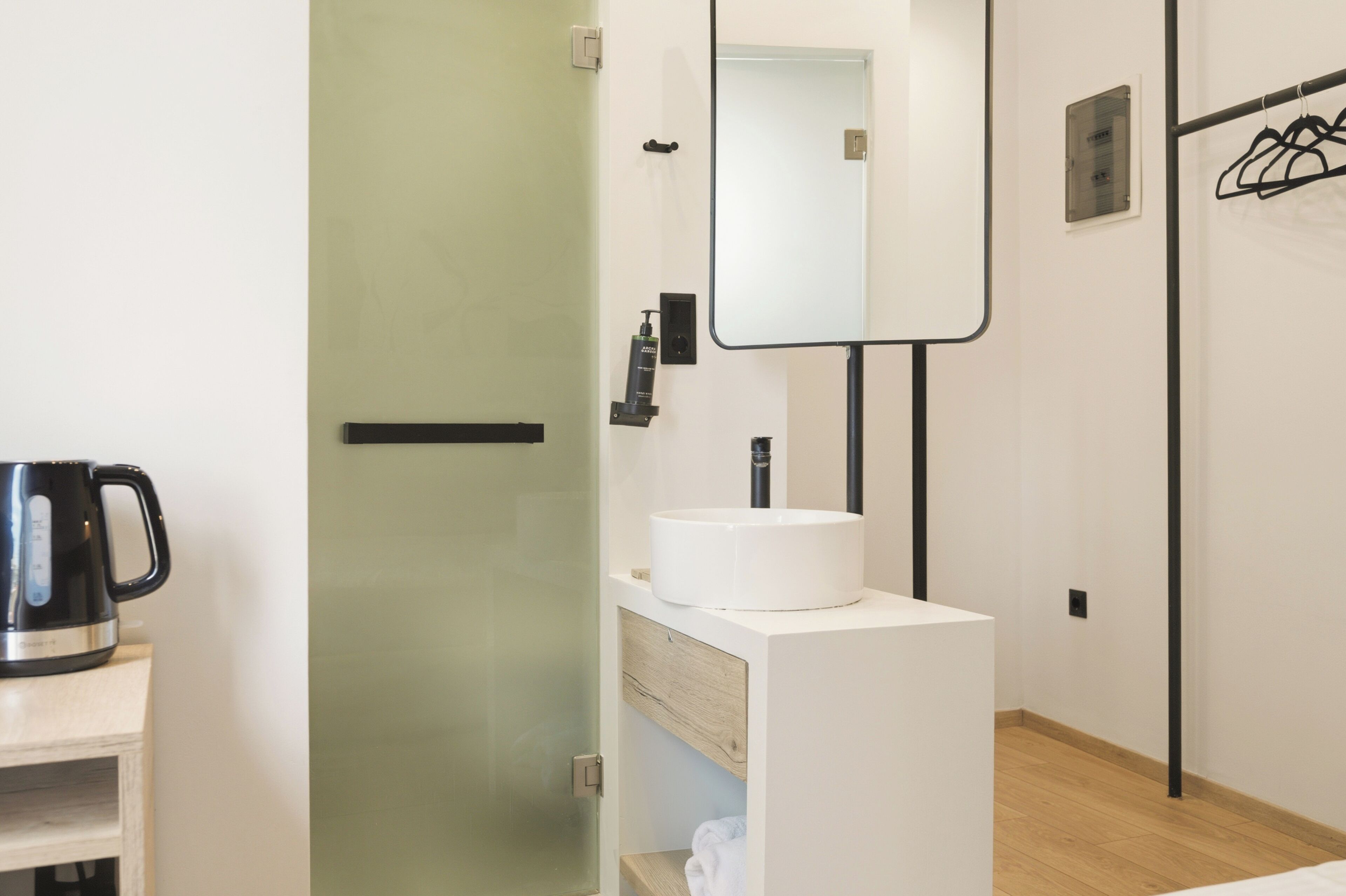 Une salle de bain moderne avec un lavabo blanc, un miroir, une machine à café noire et un porte-serviettes.