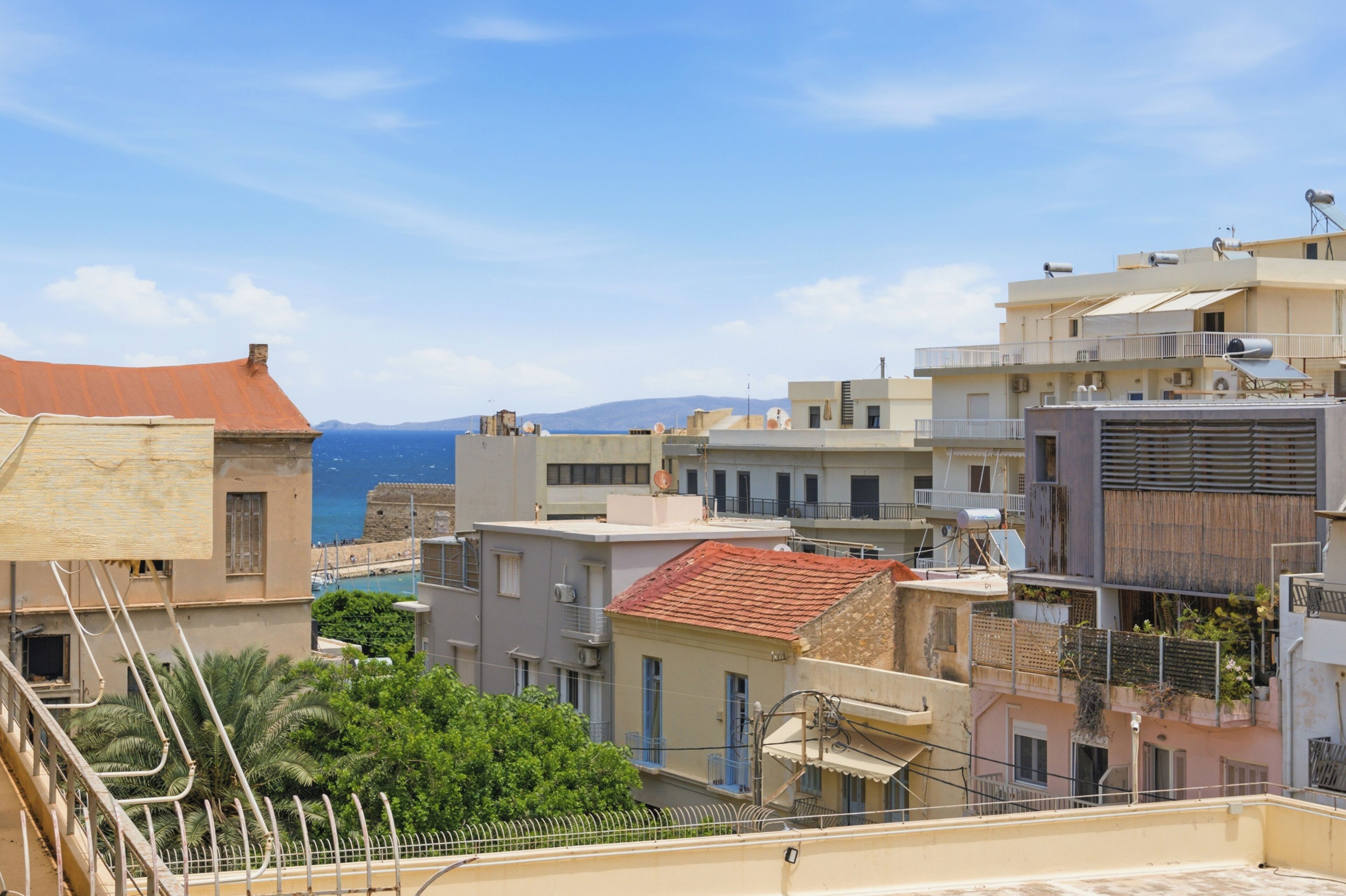 A coastal cityscape with buildings, a clear sky, and a distant view of the sea.