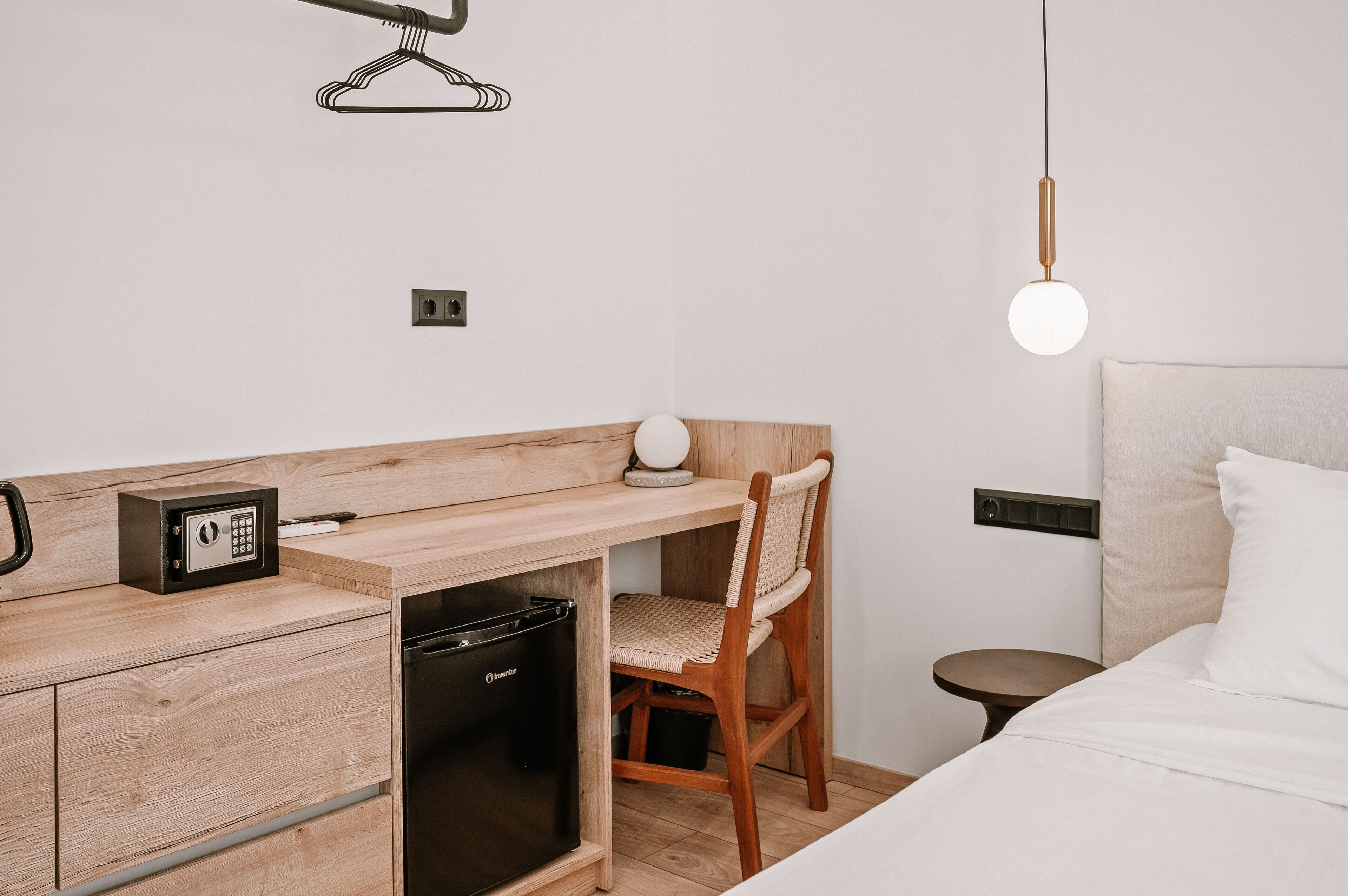 Une chambre d’hôtel compacte comprenant un bureau en bois, une chaise, un lit, une petite table de chevet et un luminaire suspendu.