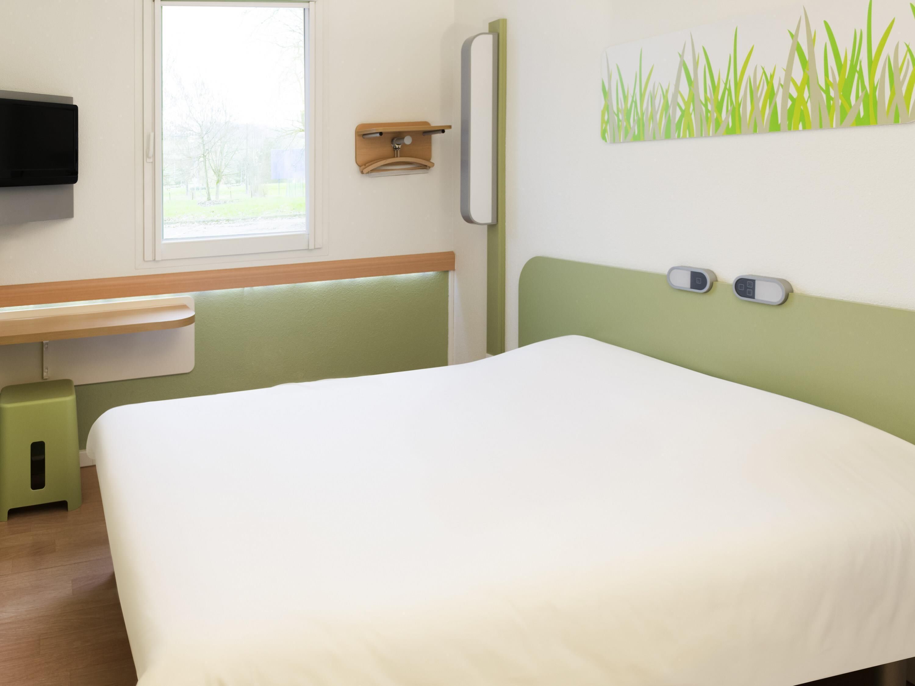 A room with a bed, a desk, a chair, a TV, and a window.