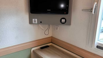 A corner room with a mounted flat-screen TV, a small stool, and a window.