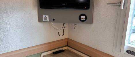 Habitación de esquina con televisor de pantalla plana montado, un taburete pequeño y una ventana.