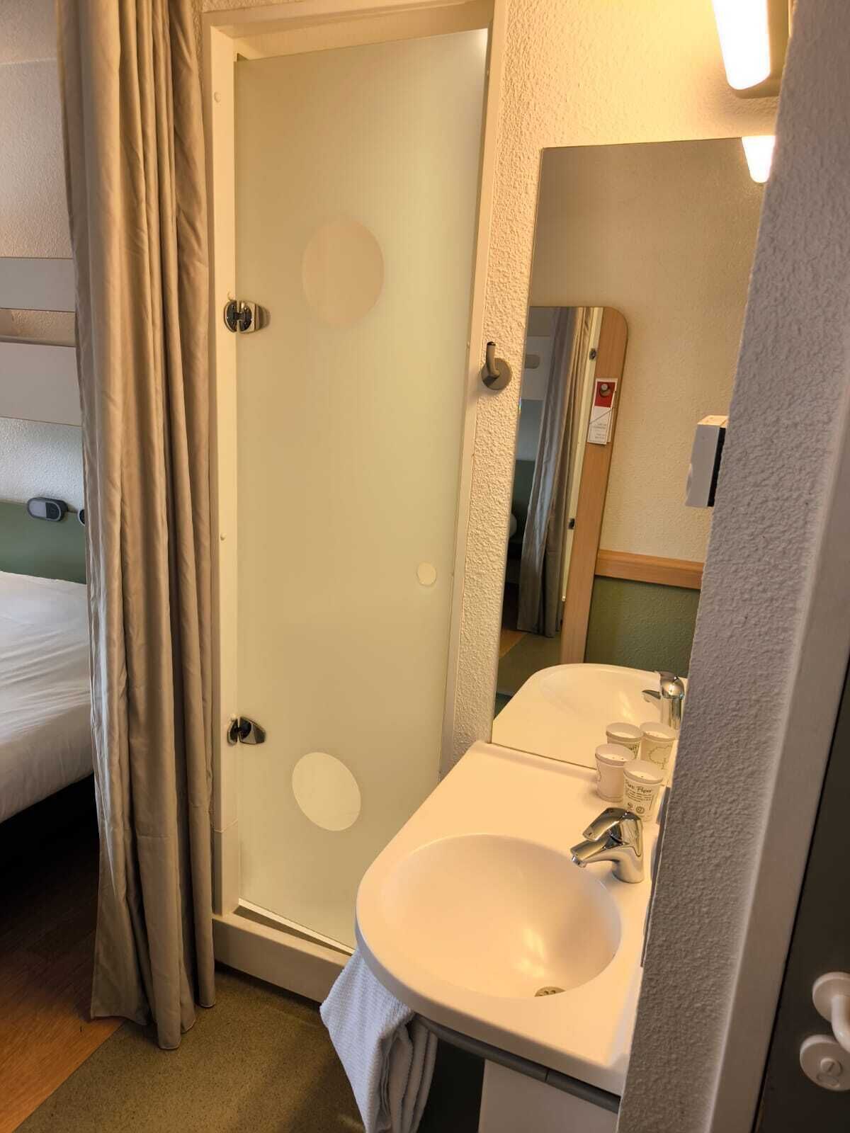 Baño con lavamanos blanco, espejo y mampara de ducha.