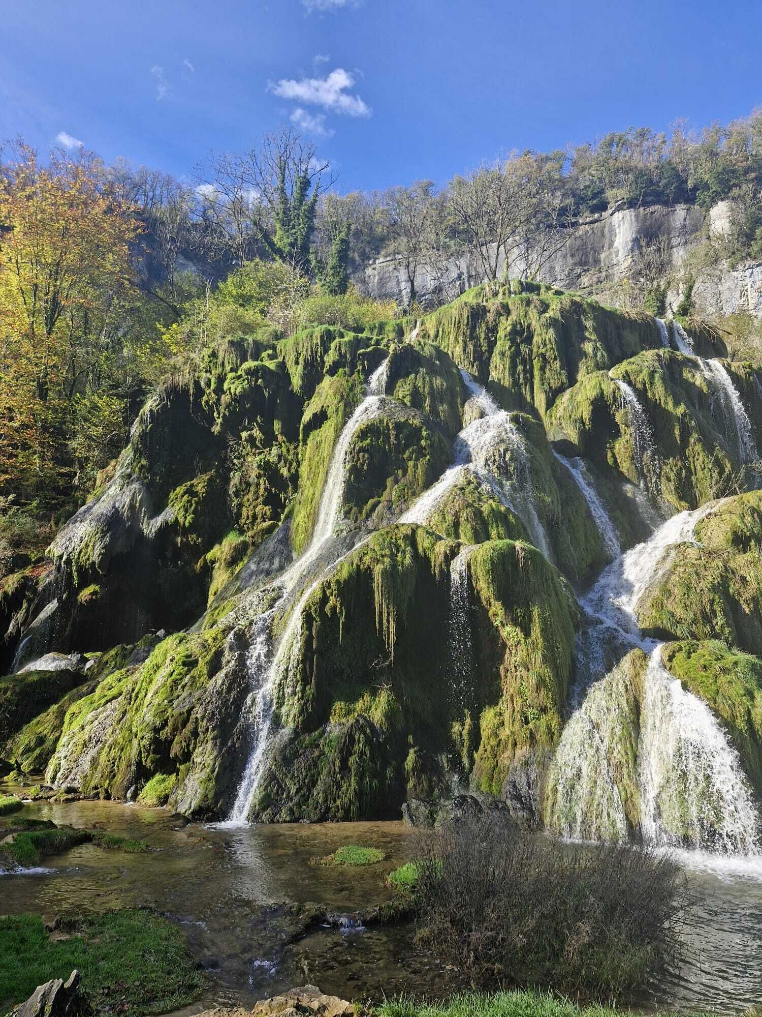 Une cascade d’eau se déversant sur des rochers couverts de mousse, avec un ruisseau aux eaux claires en contrebas.