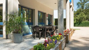 Un espace extérieur abrité, aménagé avec une table et des chaises, une plante en pot et des jardinières fleuries.