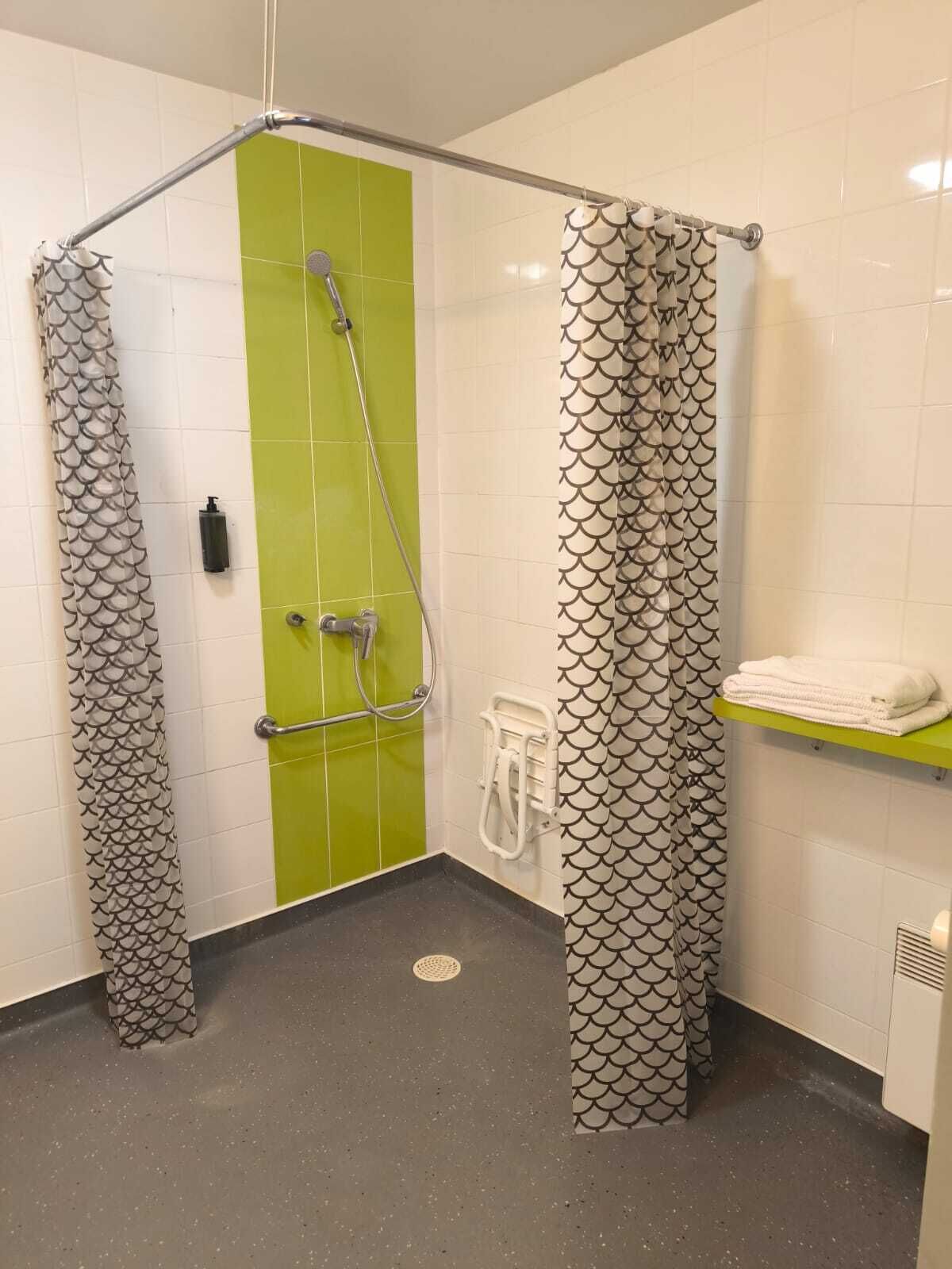 A shower area with a green wall, a white tiled floor, and a towel rack with folded towels.