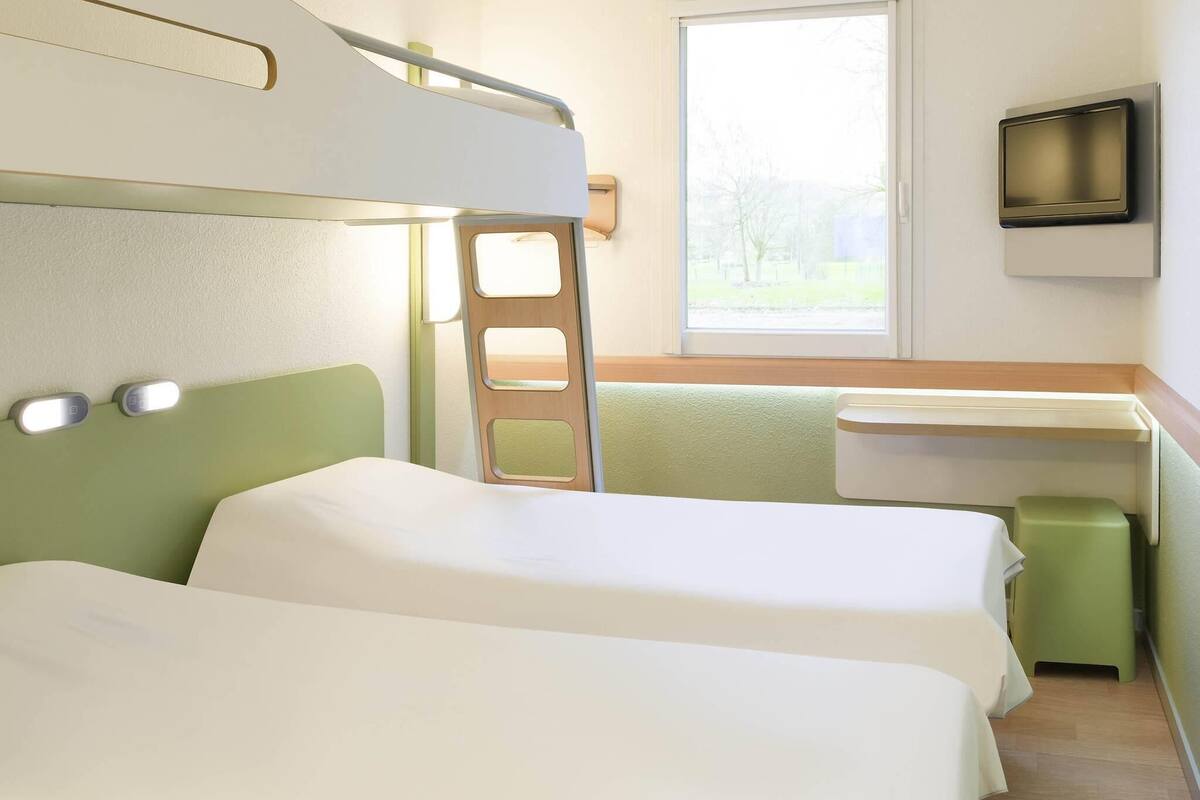 Ein Schlafraum mit Etagenbett, Fenster, Schreibtisch und Fernseher.