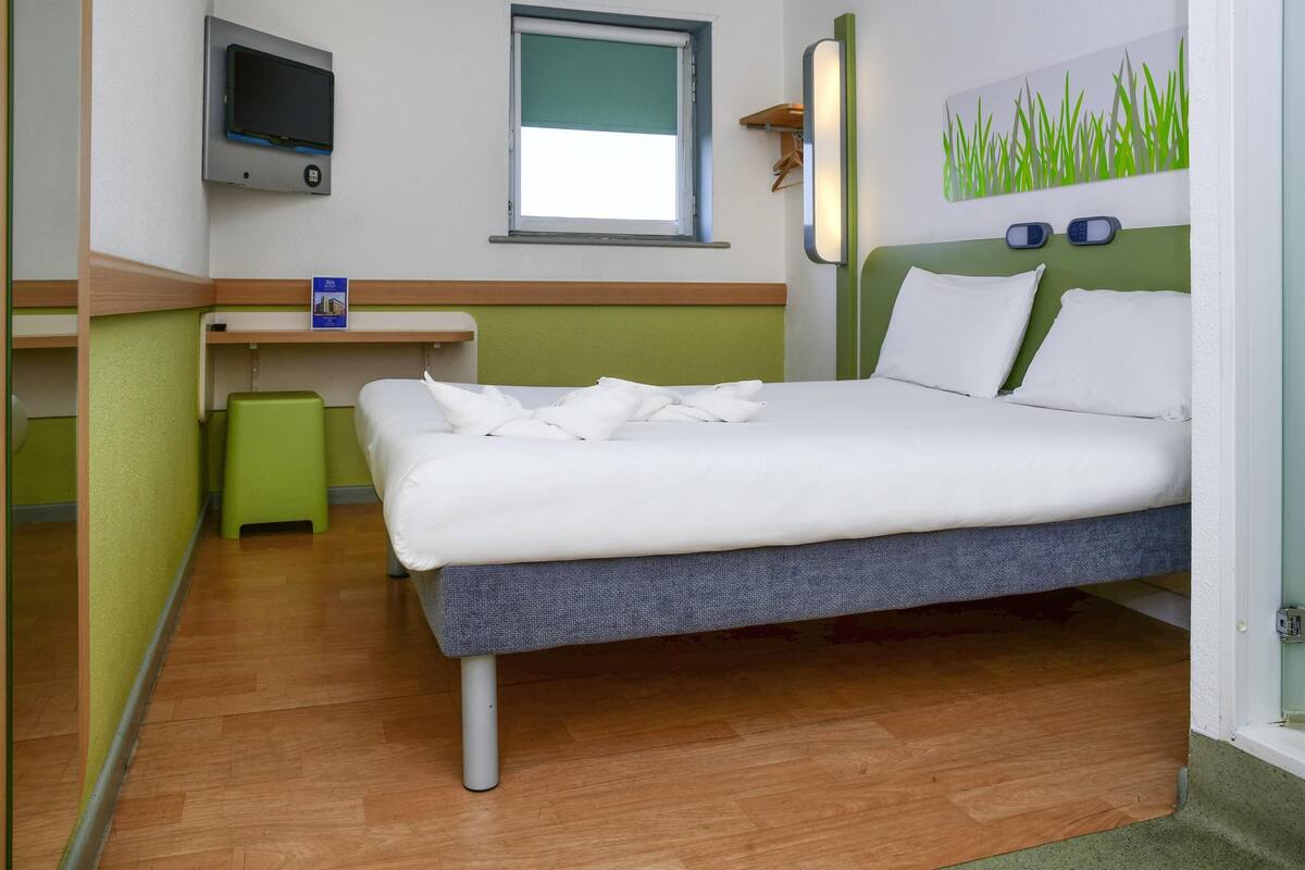 Ein Hotelzimmer mit Bett, Schreibtisch, Sessel, Fernseher und Fenster.