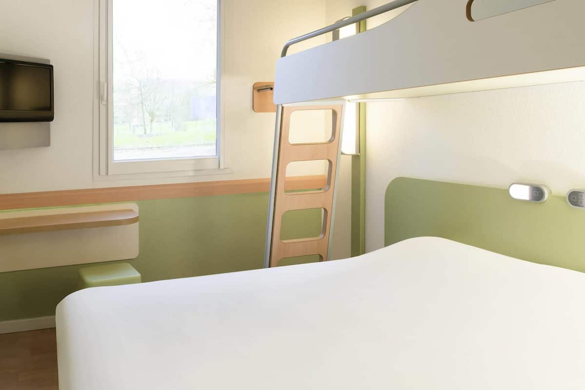 A bunk bed with a ladder, a bedside table, and a window with a view of trees.