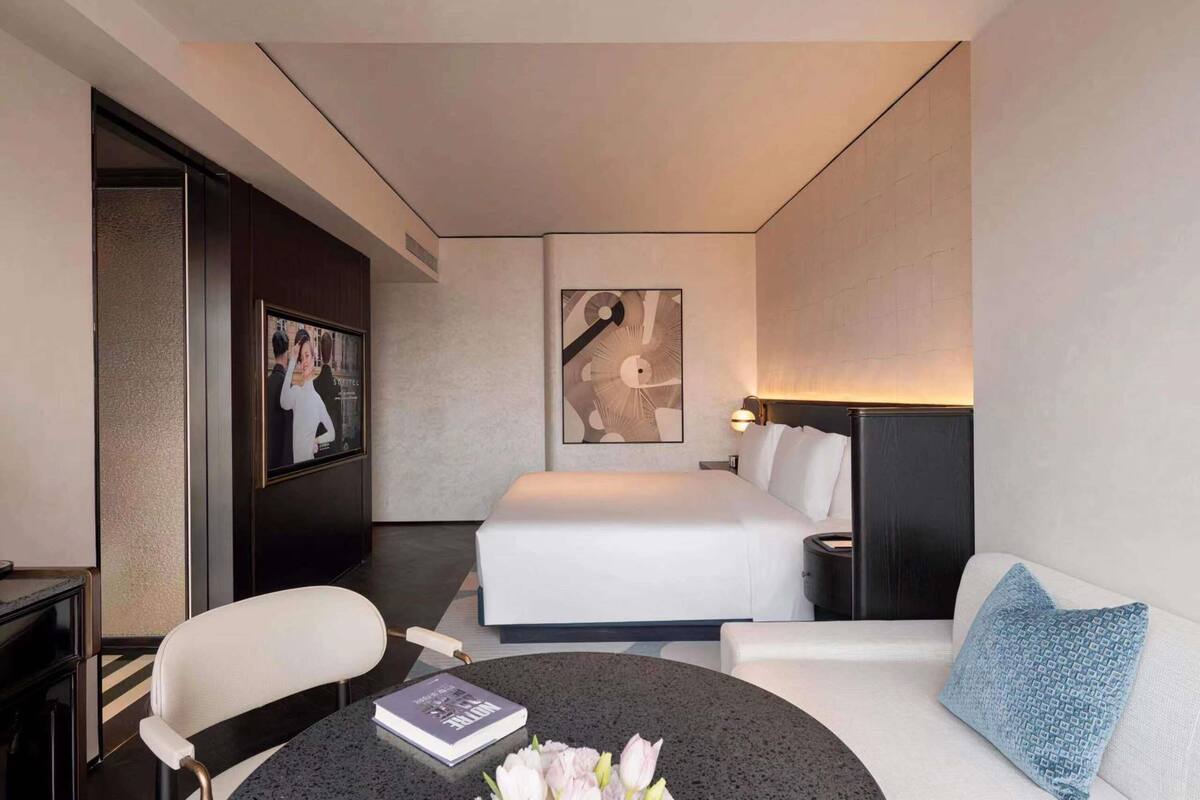 A modern hotel room with a bed, a desk, a chair, a sofa, and a coffee table.