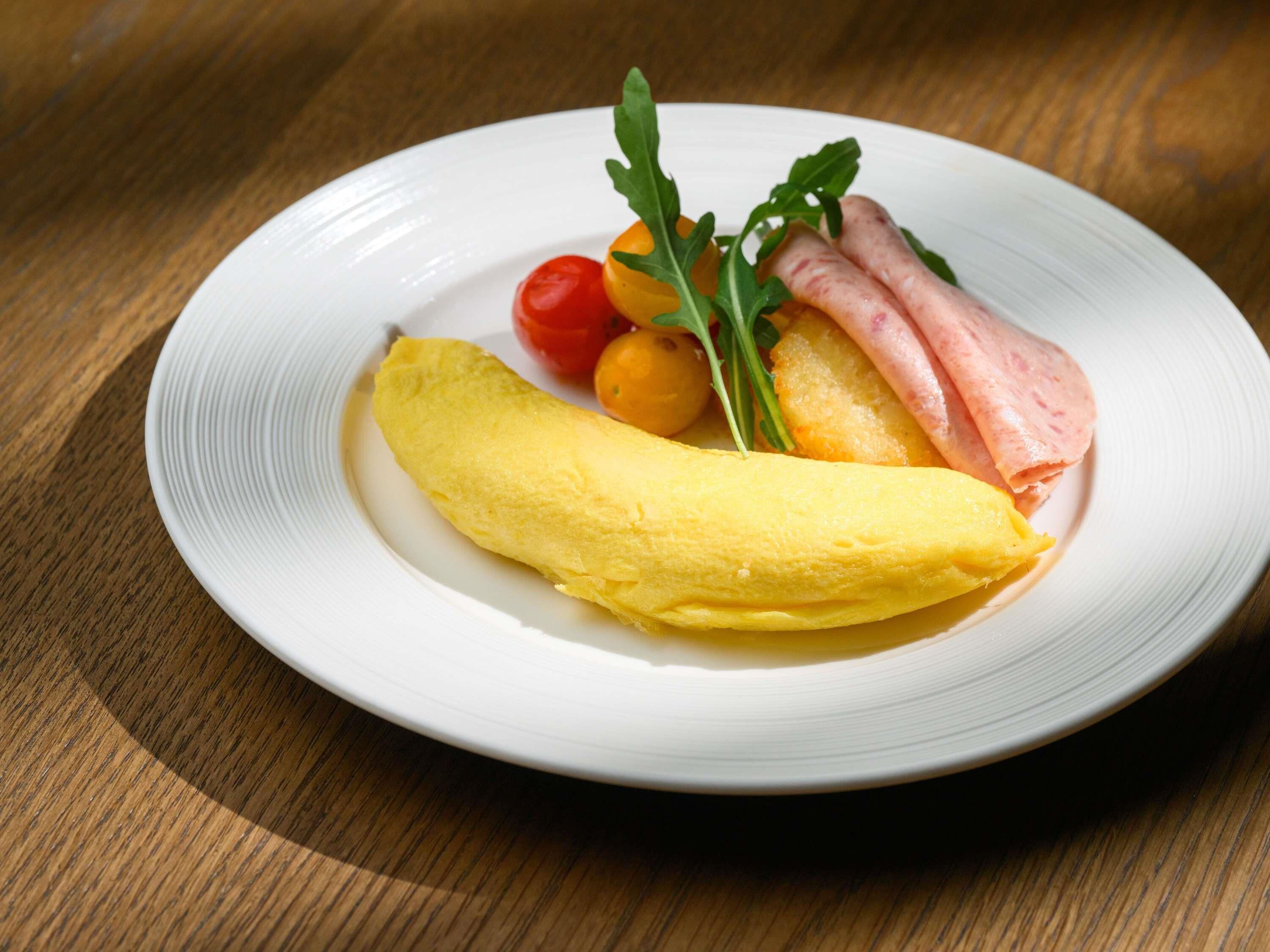 A plate with an omelette, cherry tomatoes, arugula, and ham on a white plate.