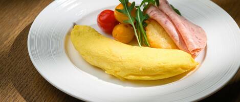 A plate with an omelette, cherry tomatoes, arugula, and ham on a white plate.