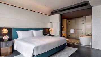 A modern hotel room with a large bed, bedside tables, a nightstand, a wall-mounted lamp, and a bathroom with a bathtub and sink.