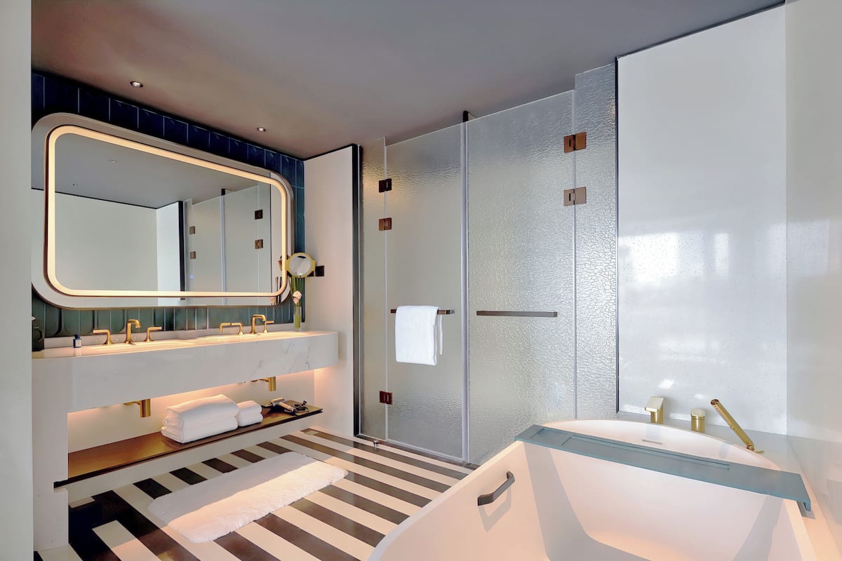 A modern bathroom with a large mirror, two sinks, a glass shower enclosure, and a striped floor.