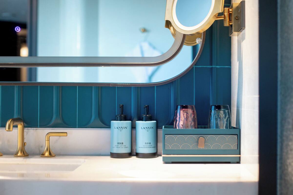 A bathroom with a white sink, two Lanvin body lotion bottles, a blue patterned soap dish, and a gold faucet.