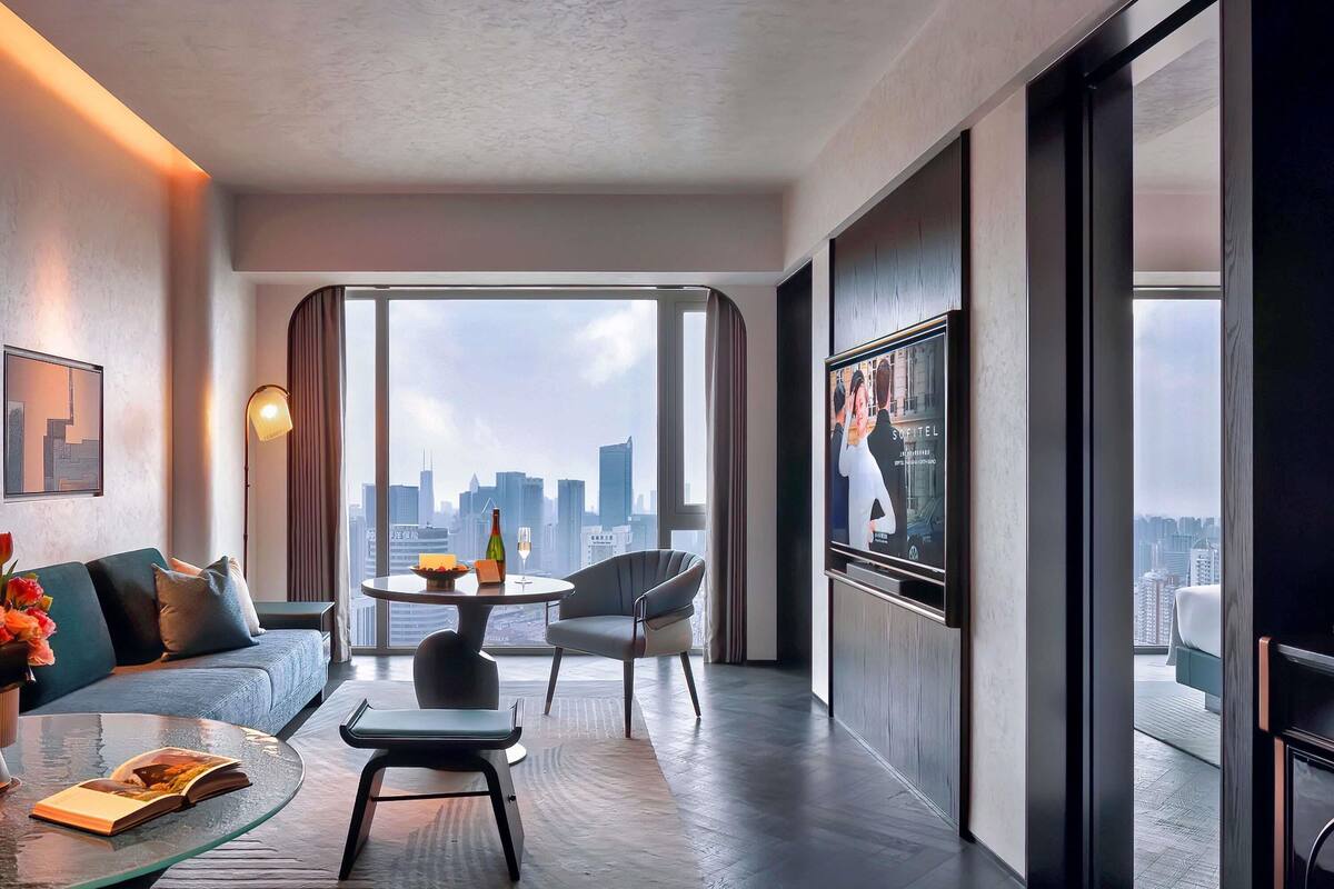 Een moderne hotelkamer met uitzicht over de stad, een bank, een salontafel, een televisie en een eethoek.