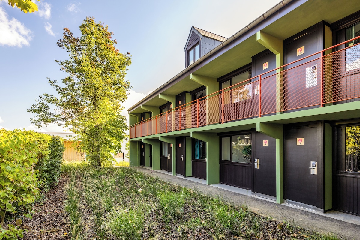 A modern building with a green facade, multiple doors, and a red railing on the upper level.