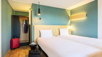 Una habitación de hotel con una cama grande, un armario, una maleta, un bolso de mano y una mesita de noche.