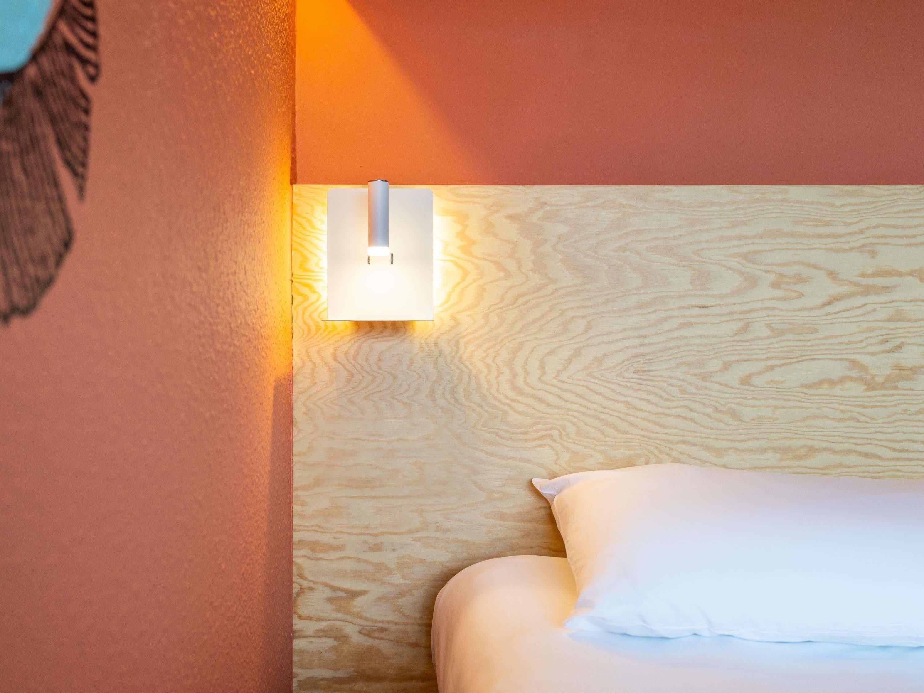 A hotel room with a wooden headboard, a white pillow, and a wall-mounted light fixture.