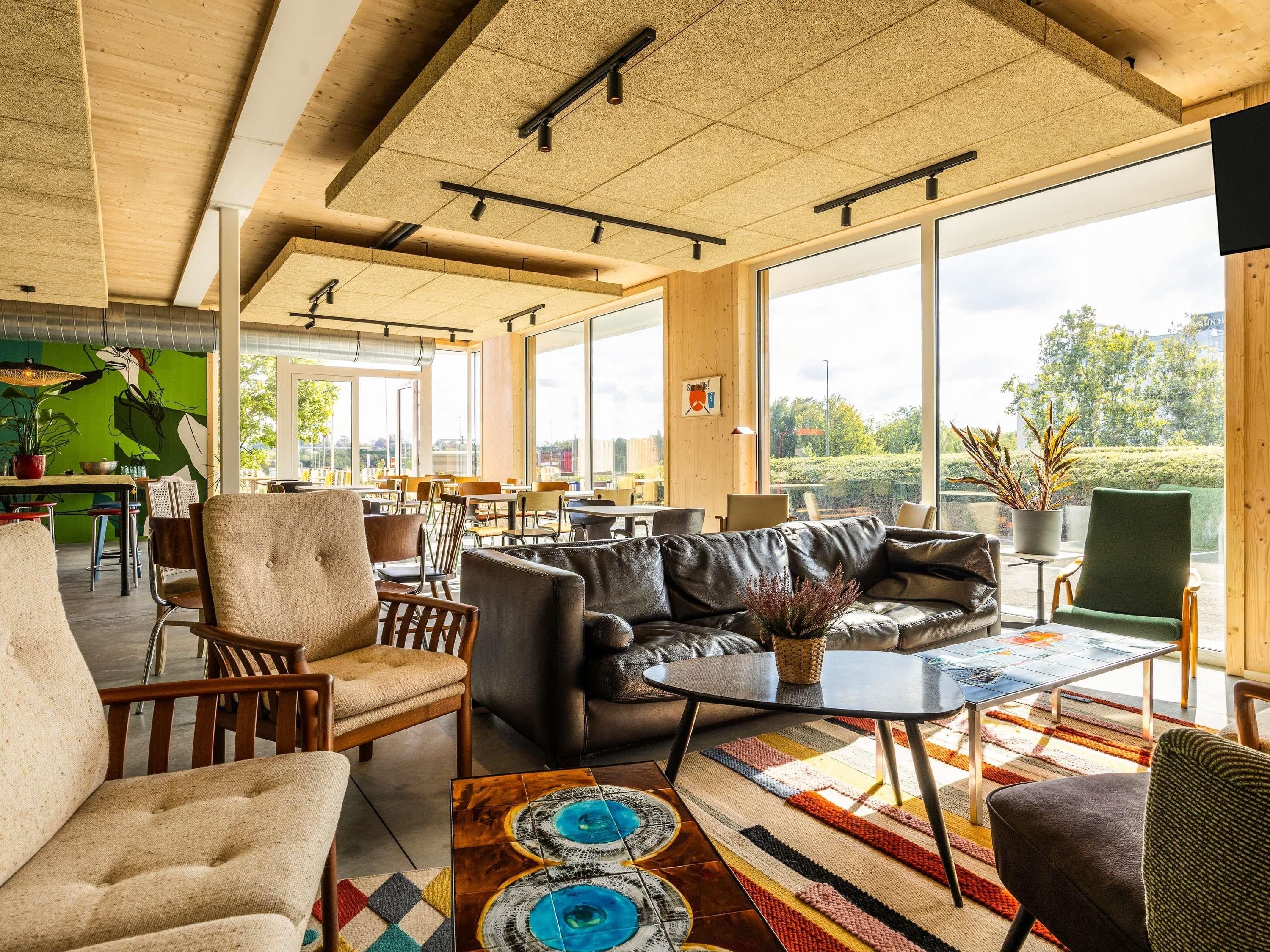 Ein modernes Interieur mit einer Couch, Sesseln, einem Couchtisch und großen Fenstern mit Blick ins Freie.