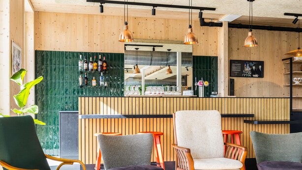 Un área de bar con paneles de madera, una barra con botellas y asientos con cojines estampados.