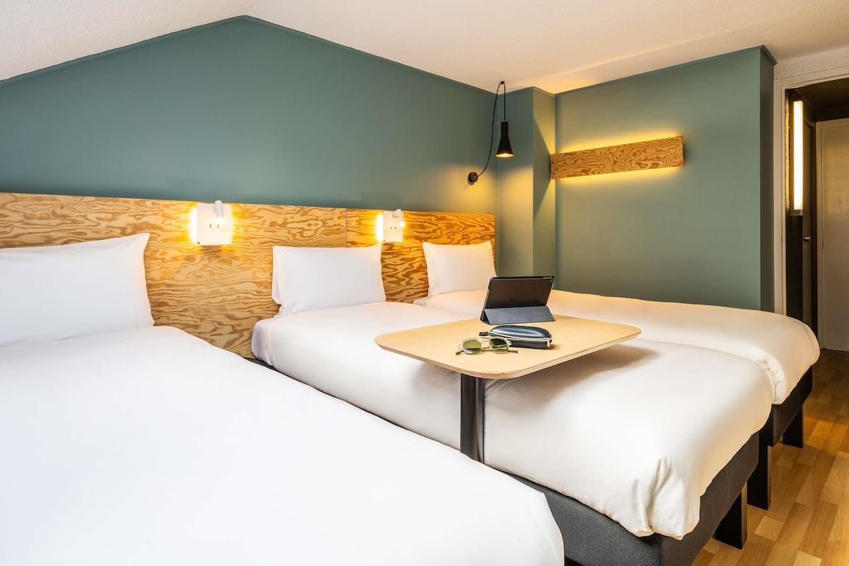 Habitación de hotel con dos camas, una mesita con una computadora portátil y una lámpara fijada a la pared.