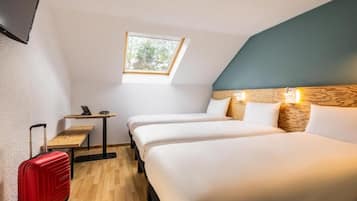 Een kamer met twee bedden, een klein tafeltje, een laptop, een rode koffer en een raam met uitzicht op bomen.