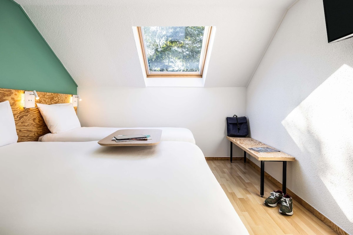 Un dormitorio con techo inclinado, tragaluz, cama, mesita de noche y un par de zapatos.