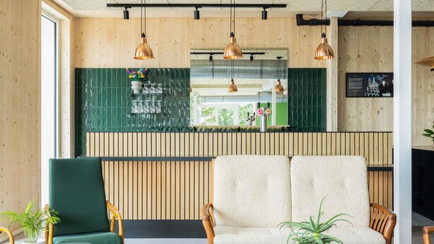 Zona de bar moderna con paneles de madera, salpicadero de azulejos verdes y un área de estar con dos sofás y una mesita.