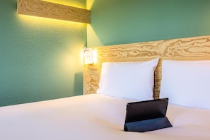 A hotel room with a bed, pillows, and a tablet on the bed. - greet Brussels Airport Zaventem (Zaventem)