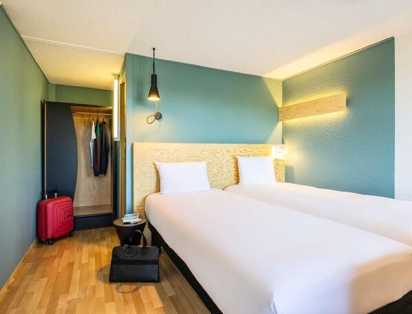 A hotel room with a double bed, a small bedside table, a red suitcase, and a closet with hanging clothes. - greet Brussels Airport Zaventem (Zaventem)