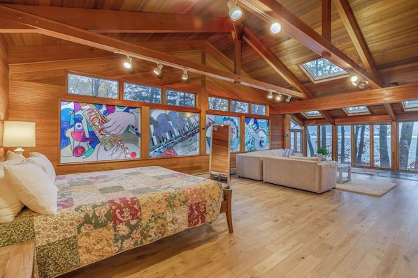 A spacious room with a large bed, a sofa, and a view of the outdoors through large windows.