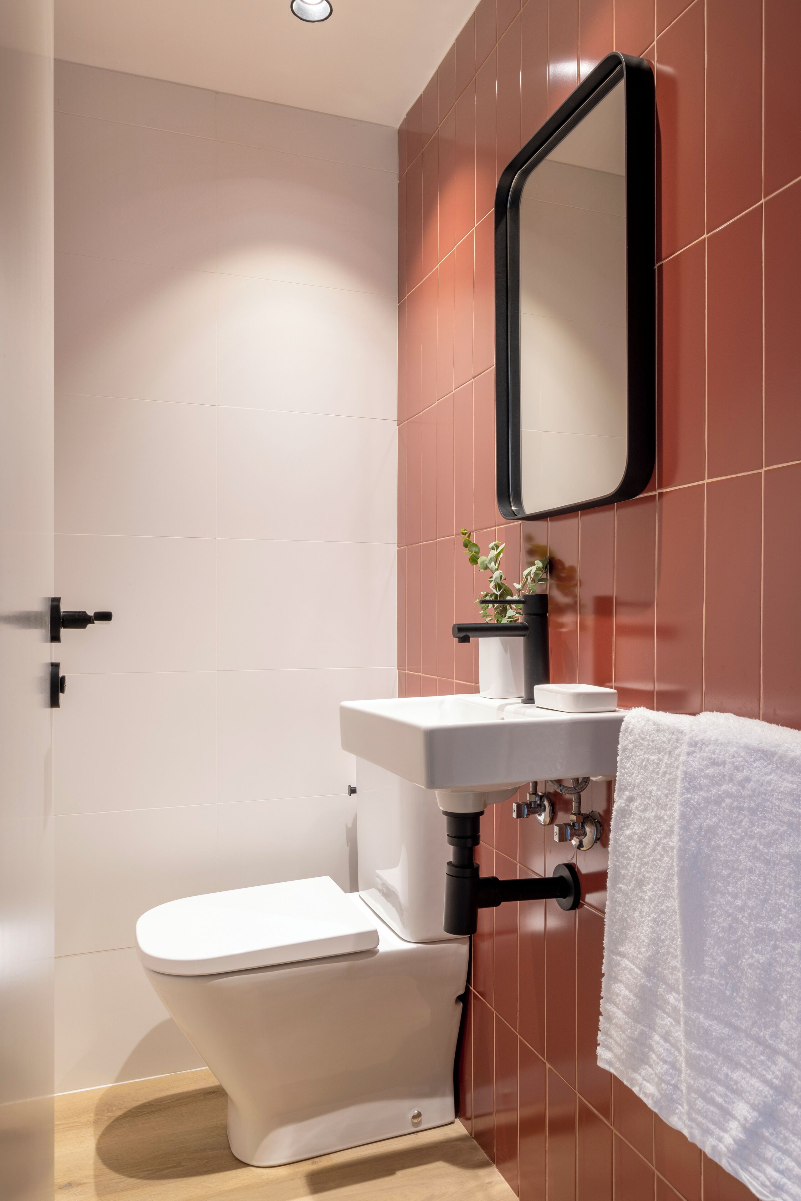 Un baño moderno con inodoro blanco, lavamanos con espejo y una toalla colgada en la pared.