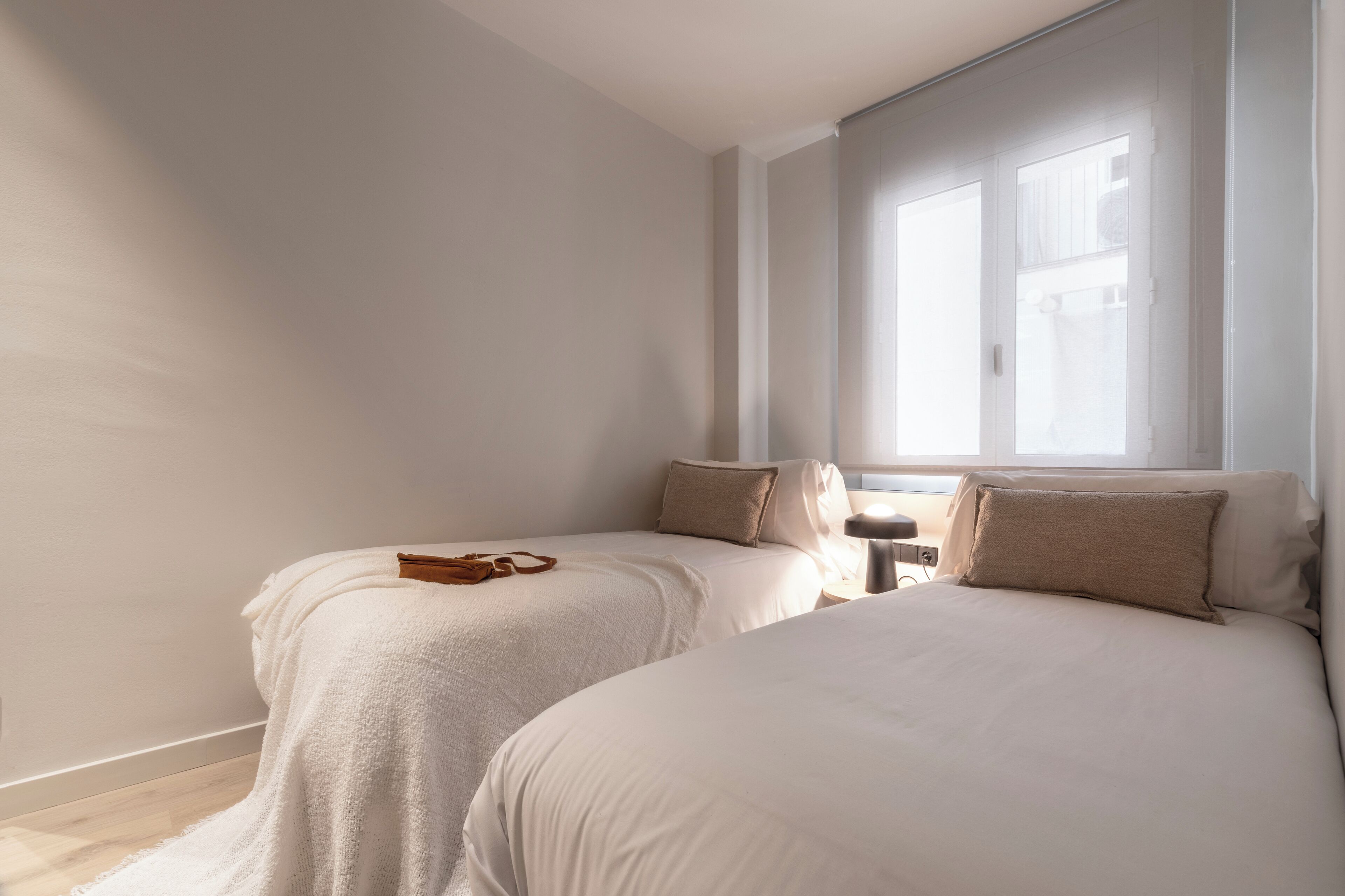 A bedroom with two beds, a nightstand, and a window with blinds.