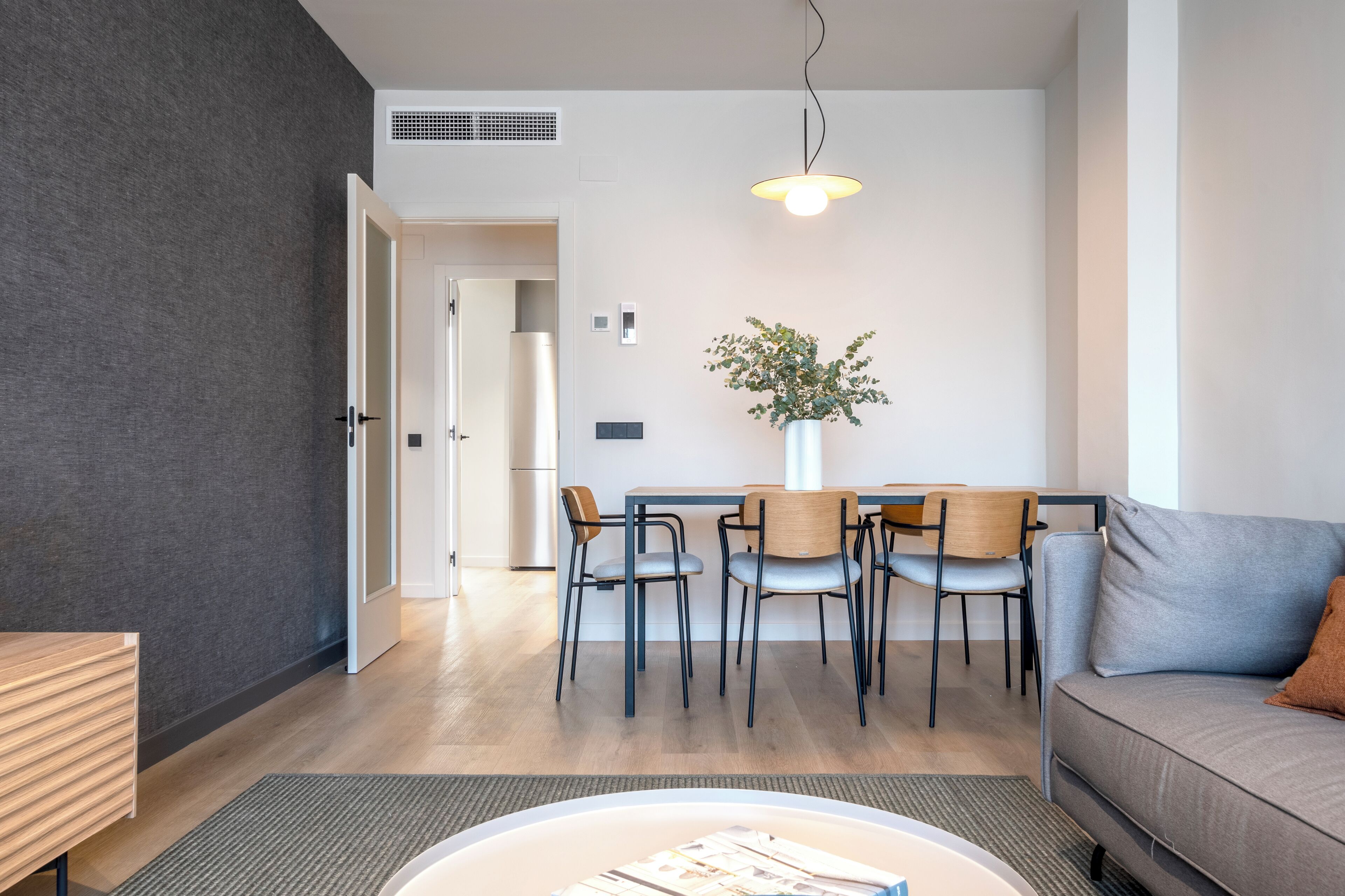 A modern living room with a sofa, dining table, chairs, a coffee table, and a hanging light fixture.