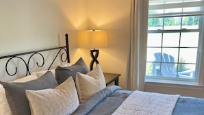 A neatly made bed with a grey and white color scheme, a bedside lamp, and a view of the outdoors through a window.