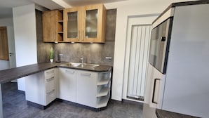 A modern kitchen with white cabinetry, a granite countertop, and a stainless steel refrigerator. - Haus am Wald Ruhig Gelegene Ferienwohnung mit Großem Garten (Bad Tabarz)