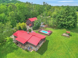 Una casa grande con techo rojo, piscina y patio cercado.