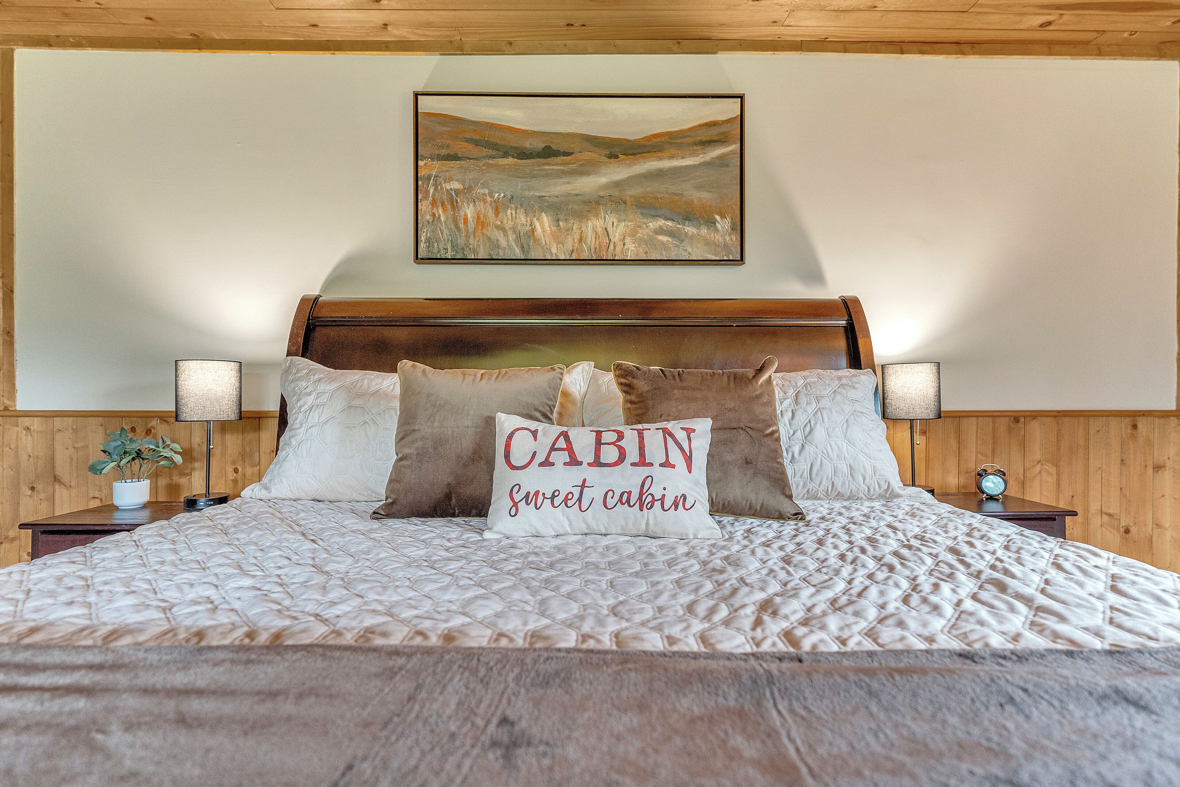 Een net opgemaakt bed met een gewatteerde deken en twee kussens, waarvan er een 'CABIN lieflijk CABIN' zegt.