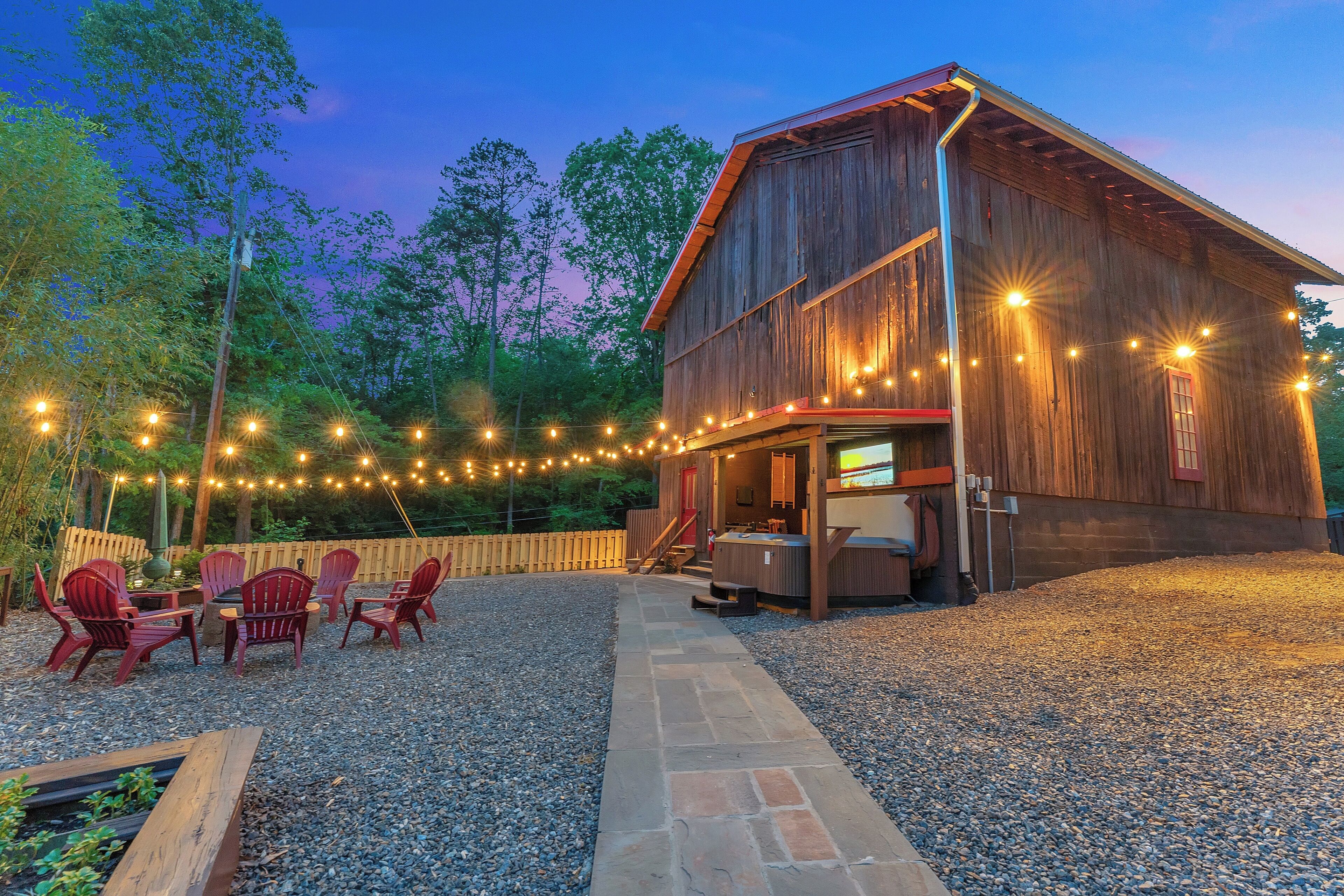 A rustic barn with string lights, outdoor seating, and a hot tub.