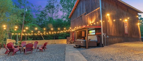 Une grange rustique décorée de guirlandes lumineuses, avec un espace salon extérieur et un jacuzzi.