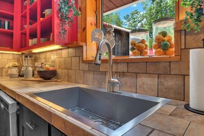 A kitchen with a stainless steel sink, a red cabinet, and a window with a view of trees.