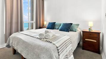 Habitación de hotel con cama, dos mesitas de noche, una ventana con cortinas y vista al mar.